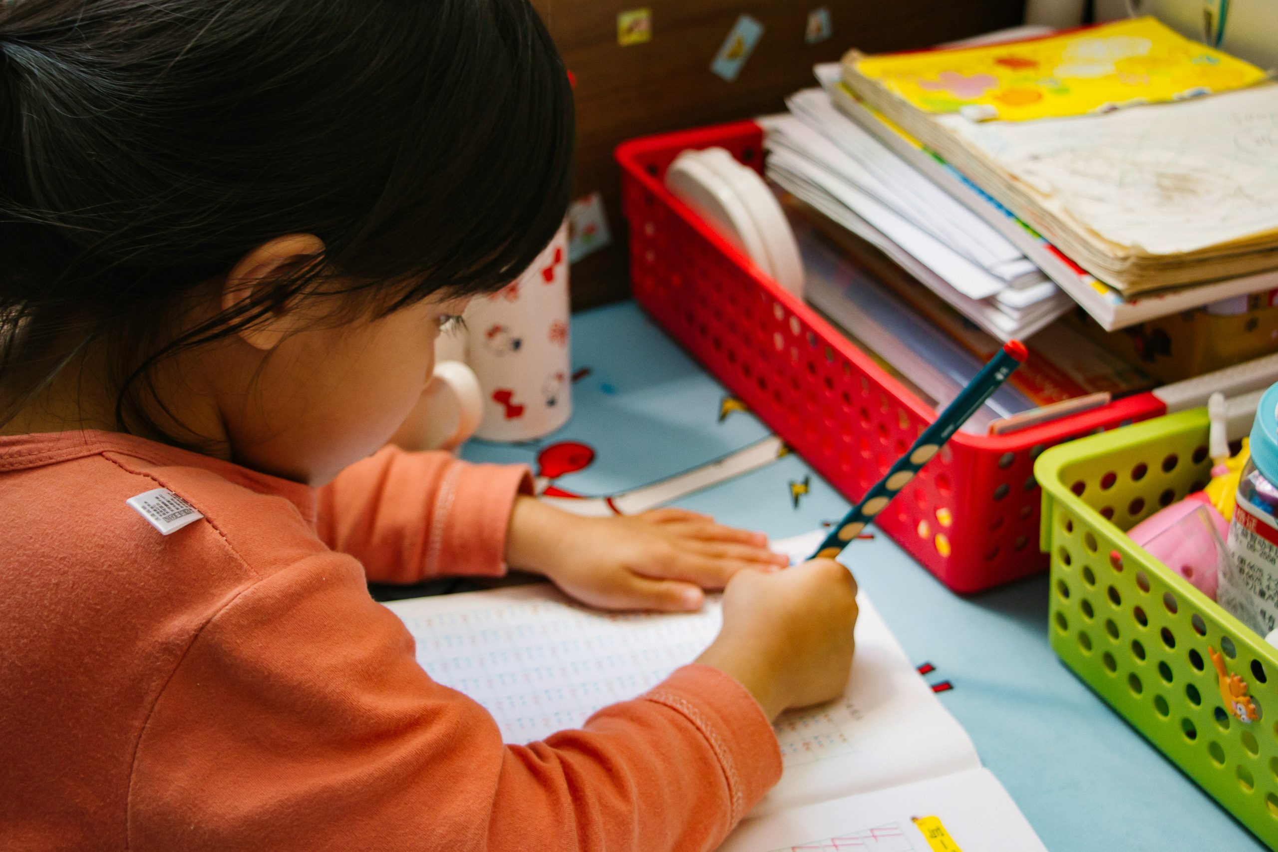 Child writing at colourful desk with pencil.