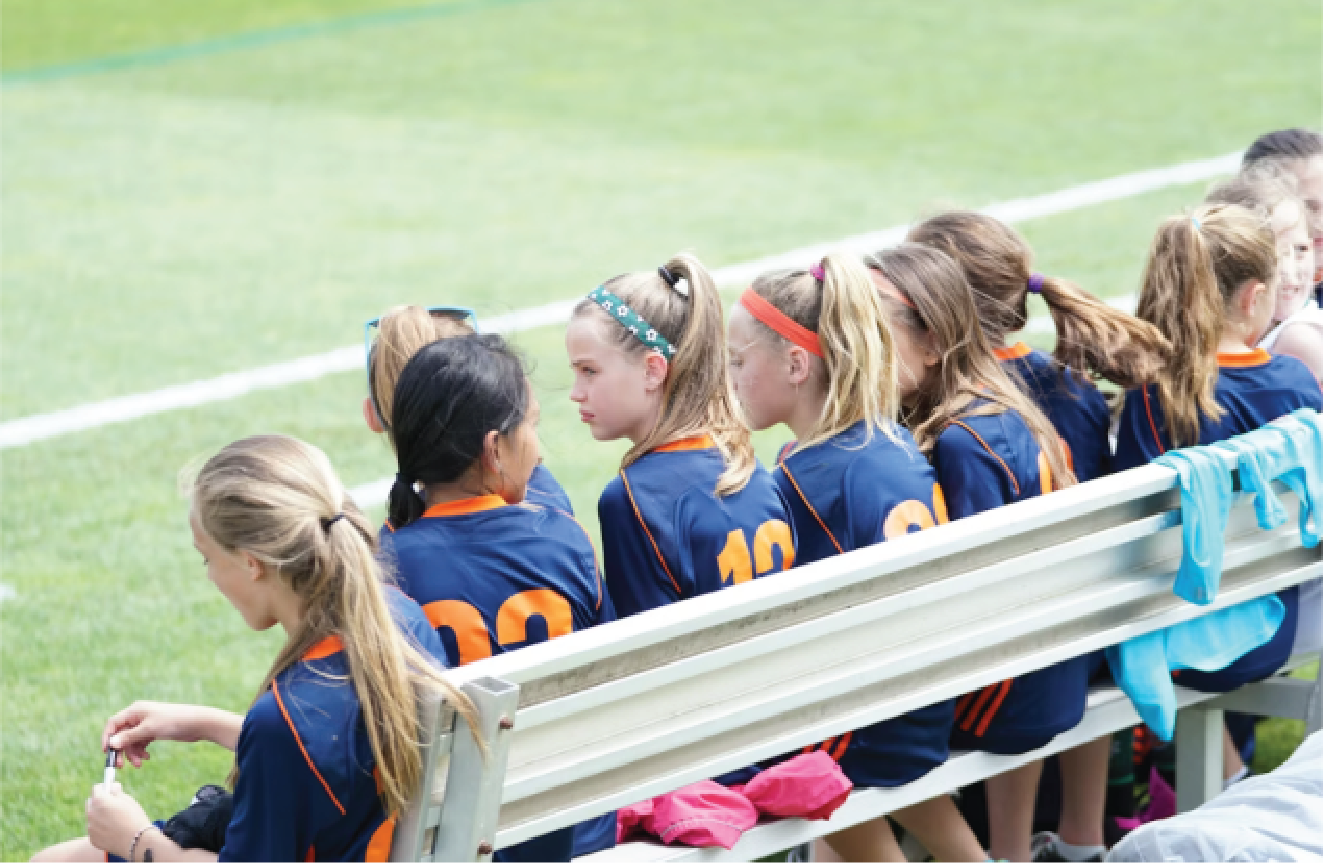 Girls in orange jerseys sitting on bench.