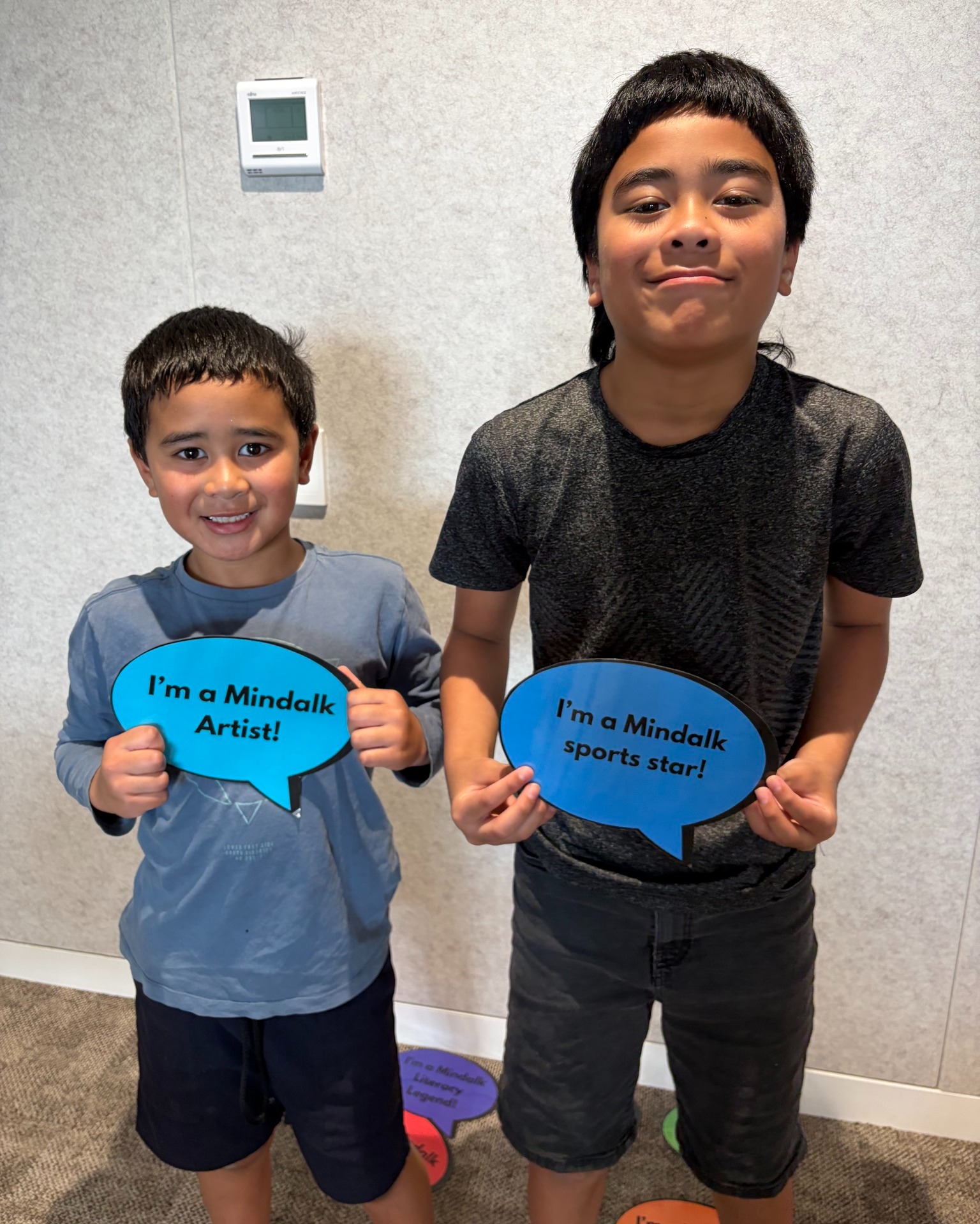 Two kids holding Mindalk signs and smiling.