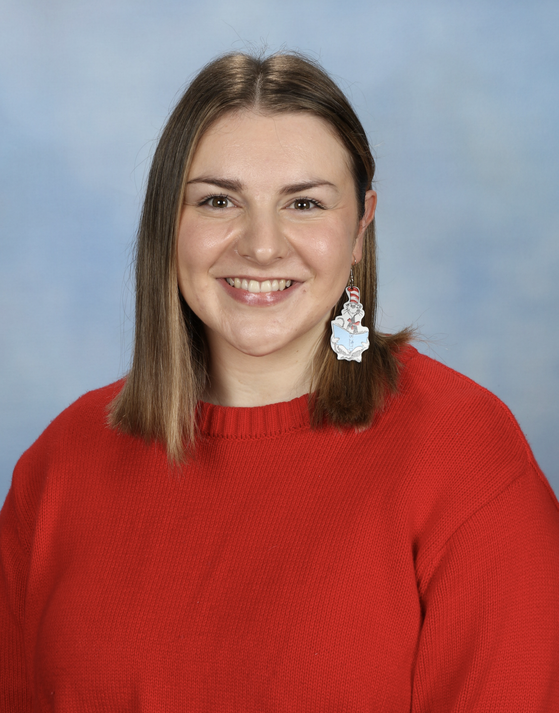 Smiling person wearing red jumper and unique earrings.