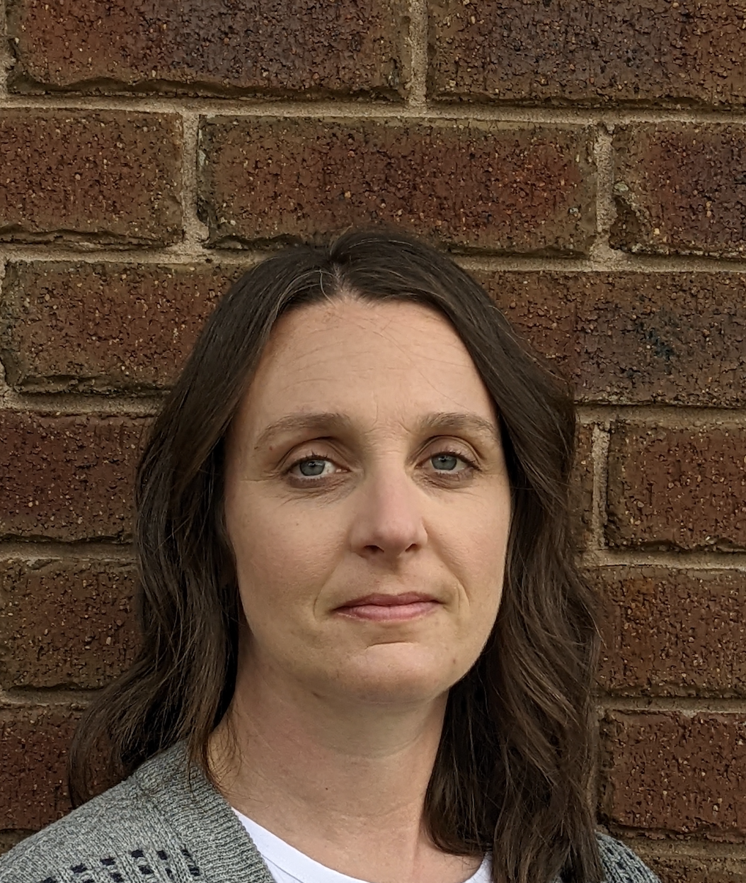 Woman standing against brick wall, neutral expression.