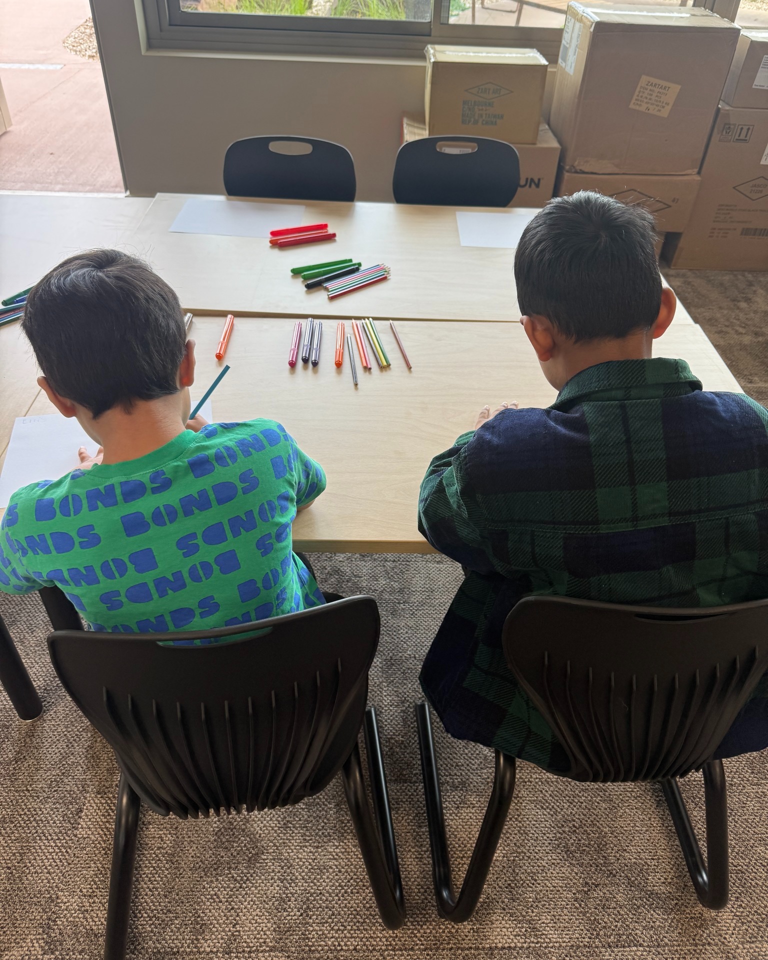 Children drawing with coloured pencils at table.