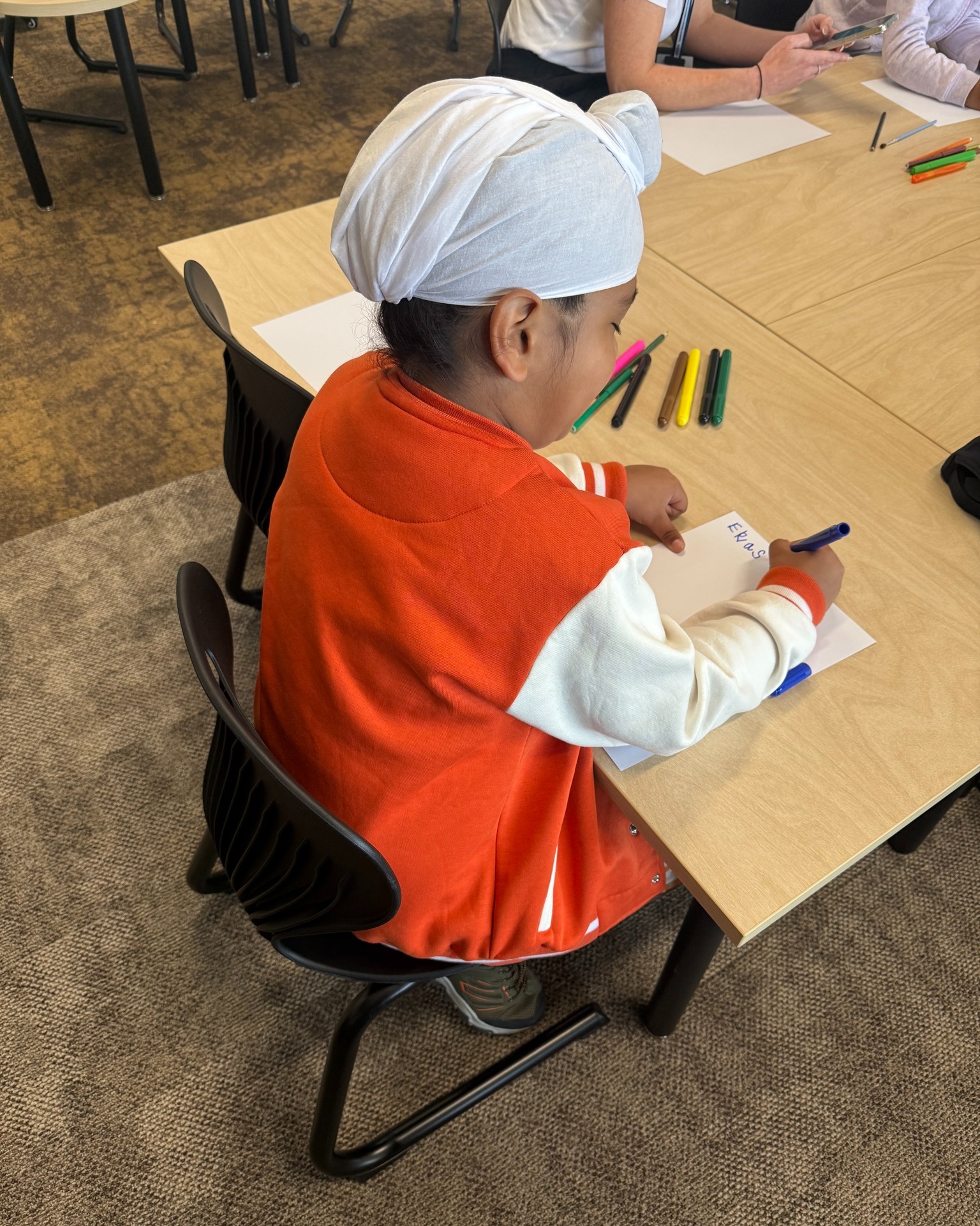 Child drawing with markers at classroom desk.