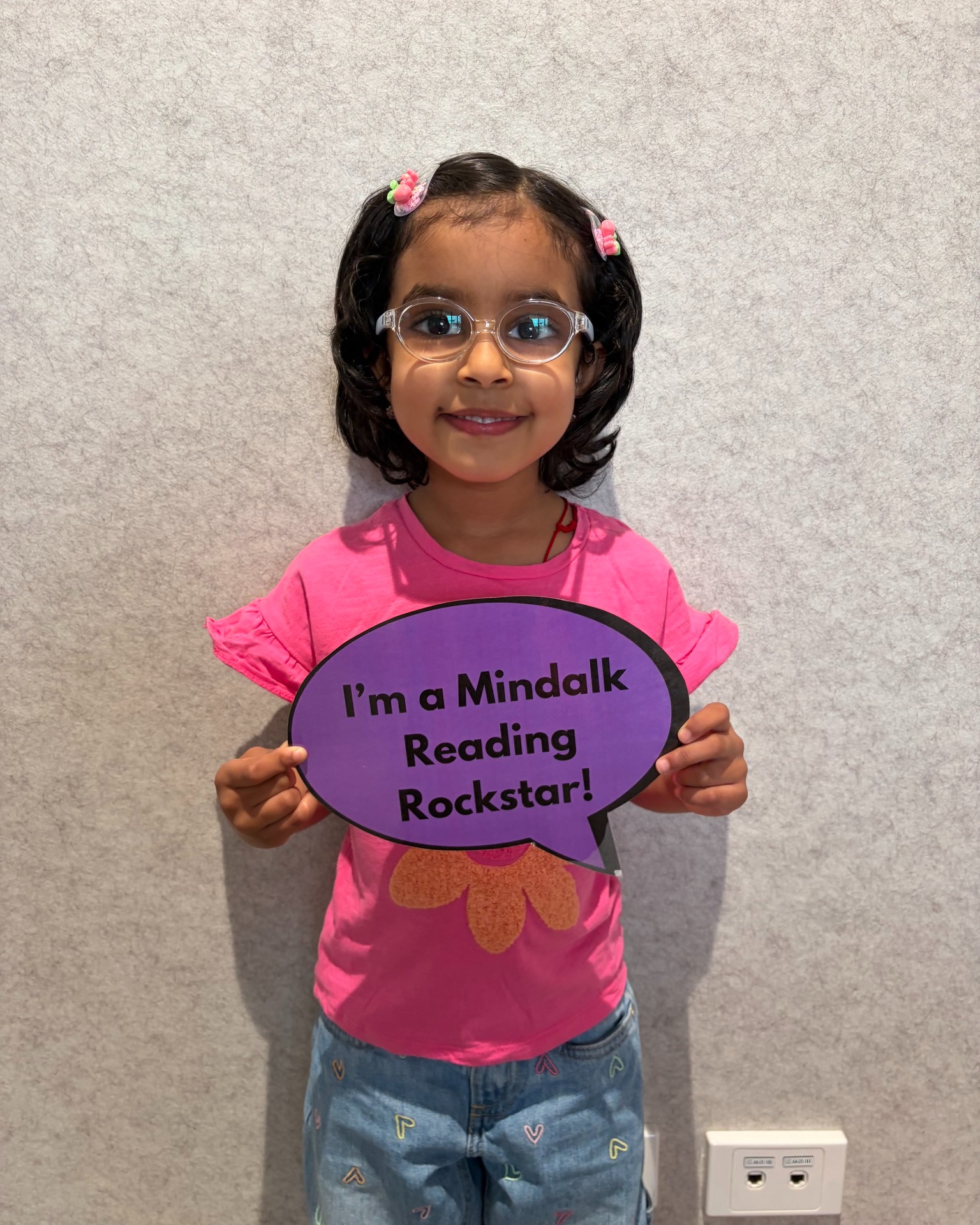 Child holding 'Mindalk Reading Rockstar' sign.