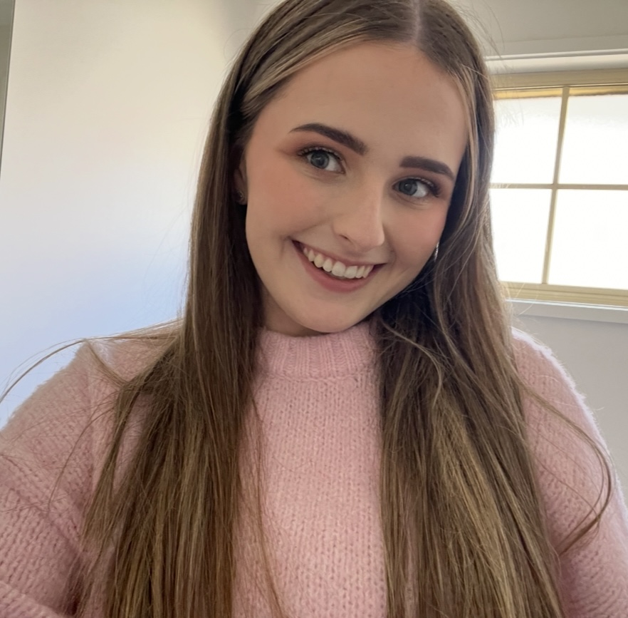 Smiling woman in pink jumper near window.